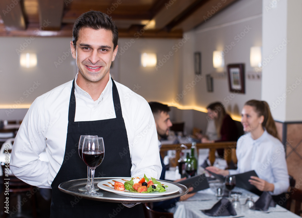 Handsome waiter with serving tray welcoming to restaurant