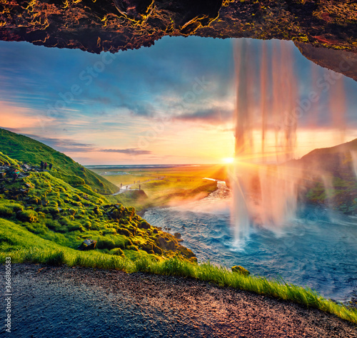 Great sunset on popular tourist destination - Seljalandsfoss waterfall, where tourists can walk behind the falling waters. Impressive summer scene of Iceland. Beauty of nature concept background.