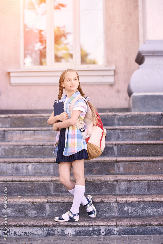 Obraz premium Young schoolgirl with backpack. Lifestyle going to classroom. Outdoor autumn park. Children learn smart. Street student. Happy preschool kid. Back to school. Near building