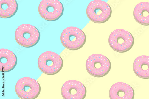 Colored pink donuts isolated on a blue and yellow background. Sweet sugar icing donuts. Snack break time with strawberry topping. Donuts top view.