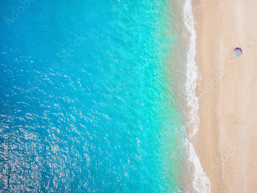 Reisekonzept mit Luftaufnahme eines leeren Strandes mit einsamen Sonnenschirm an smaragd-türkisem Meer mit Textfreiraum