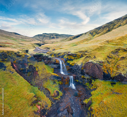View from flying drone. Majestic morning view of nameless waterfall on Rauda river. Picturesque green hills on the southern coast of Iceland at June. Beauty of nature concept background.