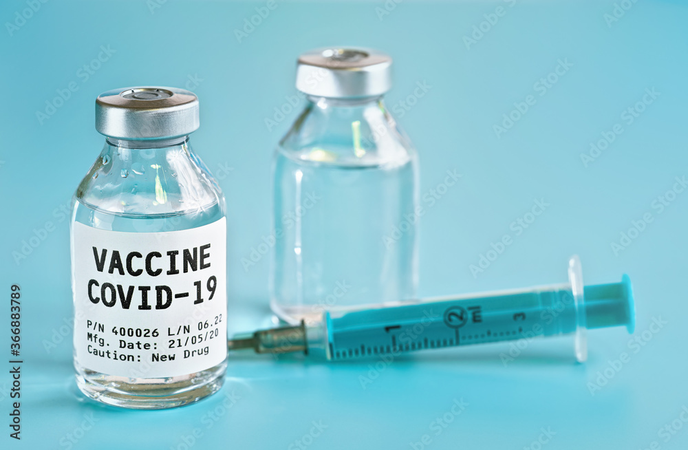 Glass vial with label Covid 19 vaccine (own design, not real product), another bottle and hypodermic syringe needle near, light blue background