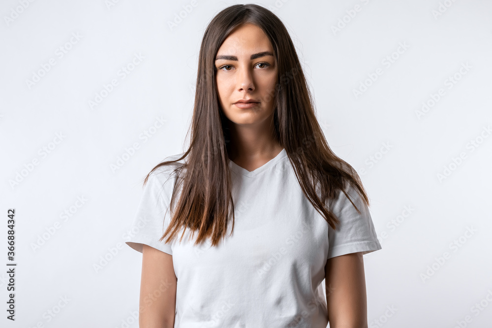 Young carefree modern girl with long chestnut hairs in casual light clothes posing isolated on white wall background. People lifestyle concept. Young carefree modern girl with long chestnut hairs in casual light clothes posing isolated on white wall background. People lifestyle concept.
