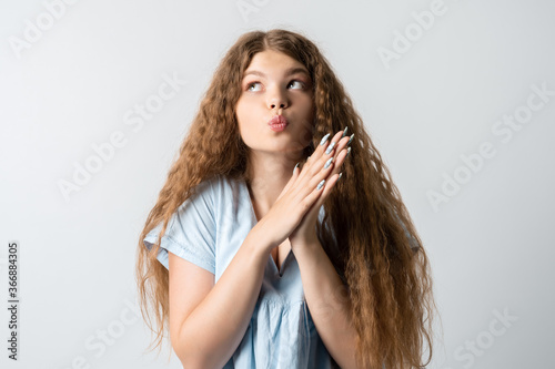 Photo of thoughtful European young woman with curly long hair looks with dreamy expression aside. Isolated over white background.