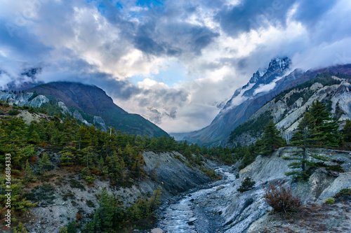 A river flowing down the mountain and glacier covered by clouds near Bhraka, Manang Nepal. A moody scenery in Annapurna Circuit trekking trail.