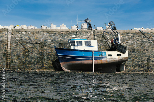 A blue fishing boat is on dry ground in the harbor at low tide