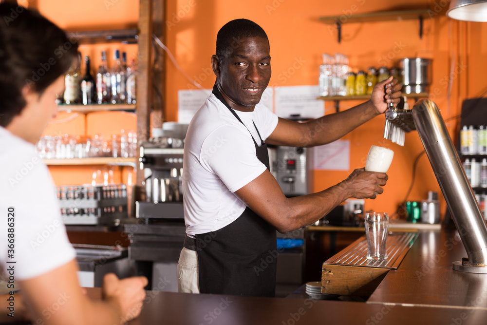 Fototapeta premium Young man barman is pouring unbottled beer for client in bar..