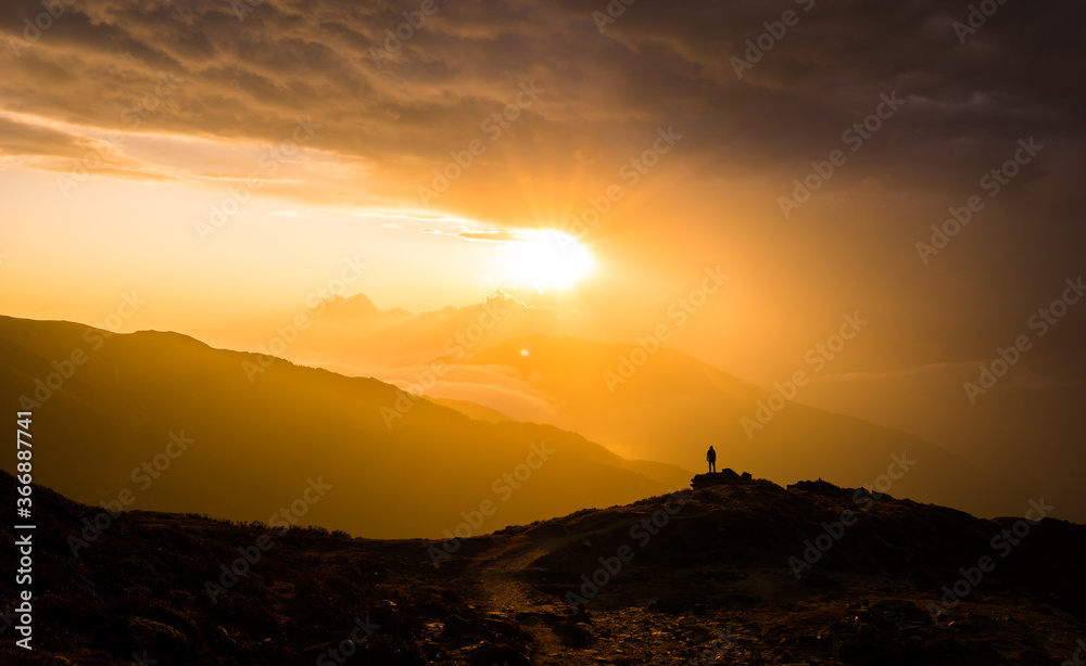 A man silhouetted against setting sun at a distance behind mountain at ...