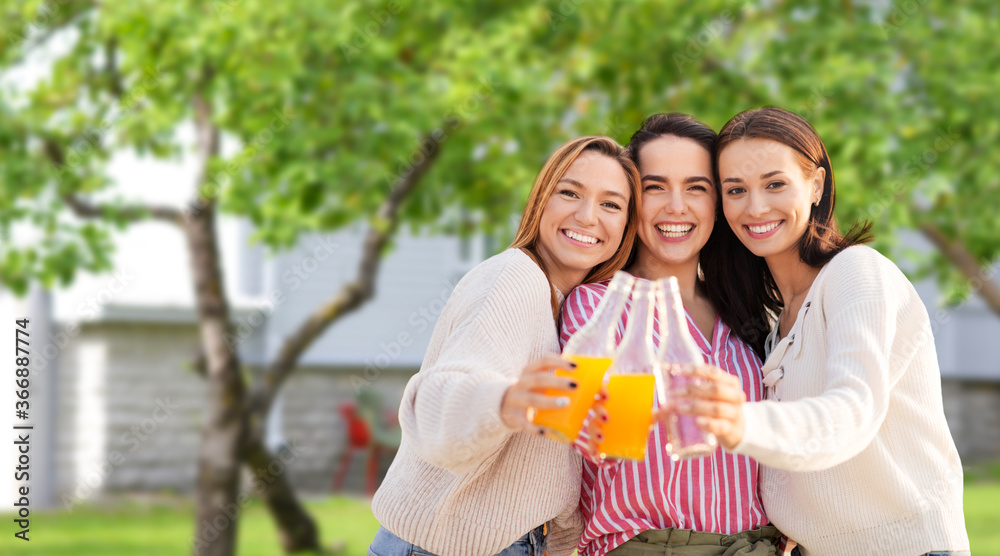 Naklejka premium friendship and leisure concept - group of happy young women or female friends toasting non alcoholic drinks over summer garden background