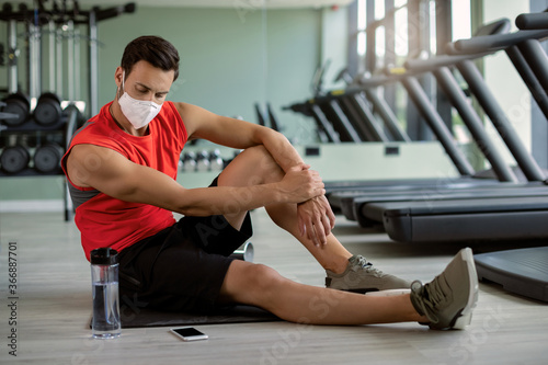 Young athletic man with face mask taking a break while having sports training in a gym