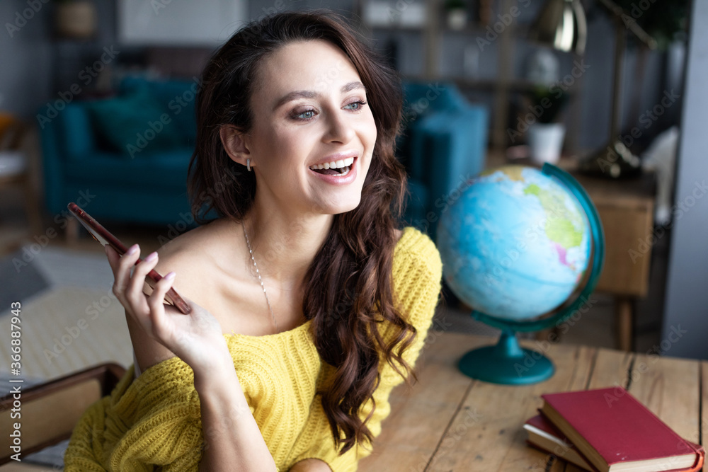 Naklejka premium Laughing woman with smartphone in the living room against the background of the world globe. Online tour booking/