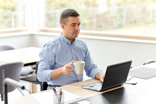 remote job, business and people concept - middle-aged man with laptop computer working at home office and drinking coffee © Syda Productions