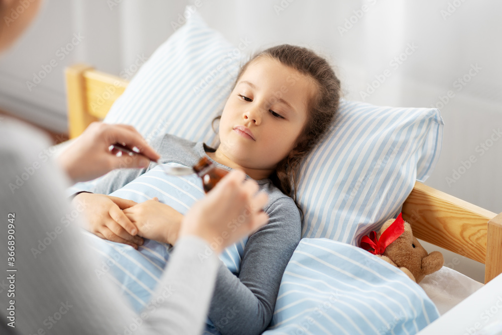 family, health and medicine concept - mother pouring cough syrup for little sick daughter lying in bed at home family, health and medicine concept - mother pouring cough syrup for little sick daughter lying in bed at home