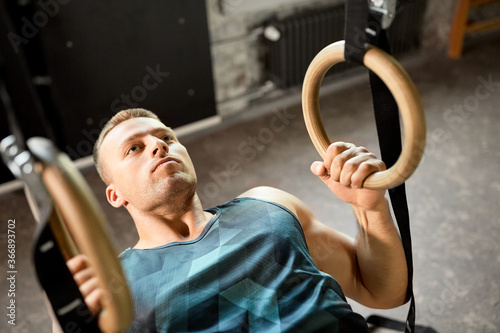 fitness, sport, bodybuilding and people concept - young man exercising on gymnastic rings in gym