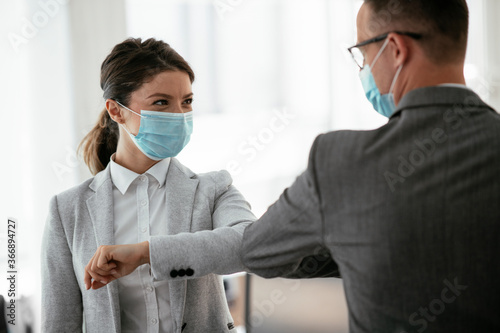 Businessman and businesswoman with medical mask in office. Greetings in Covid-19 time. 
