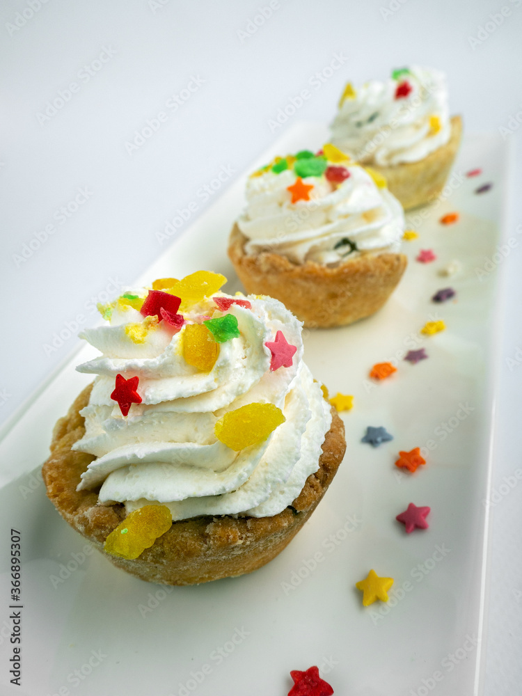 Three pastries on a platter isolated on a white background. The baskets are made of shortcrust pastry. Creamy, curd or protein cream on top. The cakes is decorated with marmalade and pastry stars. Three pastries on a platter isolated on a white background. The baskets are made of shortcrust pastry. Creamy, curd or protein cream on top. The cakes is decorated with marmalade and pastry stars.