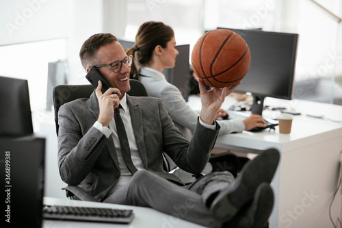 Businessman talking to the phone. Handsome businessman with basketball in office. 