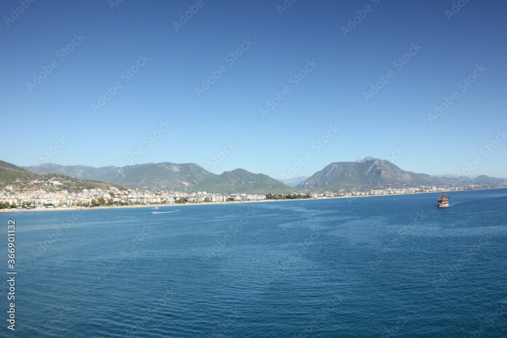 Alanya, TURKEY - August 10, 2013: Travel to Turkey. Rocks, wildlife of Turkey. Clear blue sky. The waves of the Mediterranean Sea. Water surface. Mountains and hills in the distance in the background.