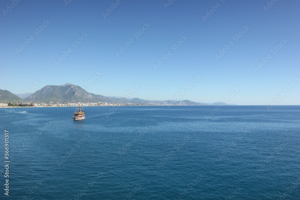 Alanya, TURKEY - August 10, 2013: Travel to Turkey. Rocks, wildlife of Turkey. Clear blue sky. The waves of the Mediterranean Sea. Water surface. Mountains and hills in the distance in the background.