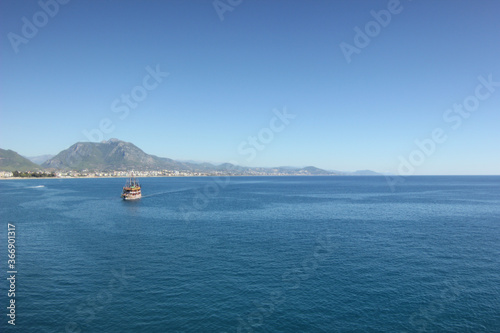 Alanya, TURKEY - August 10, 2013: Travel to Turkey. Rocks, wildlife of Turkey. Clear blue sky. The waves of the Mediterranean Sea. Water surface. Mountains and hills in the distance in the background. © andreswestrum