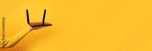 black wifi router on female hand over yellow background, panoramic mock-up image