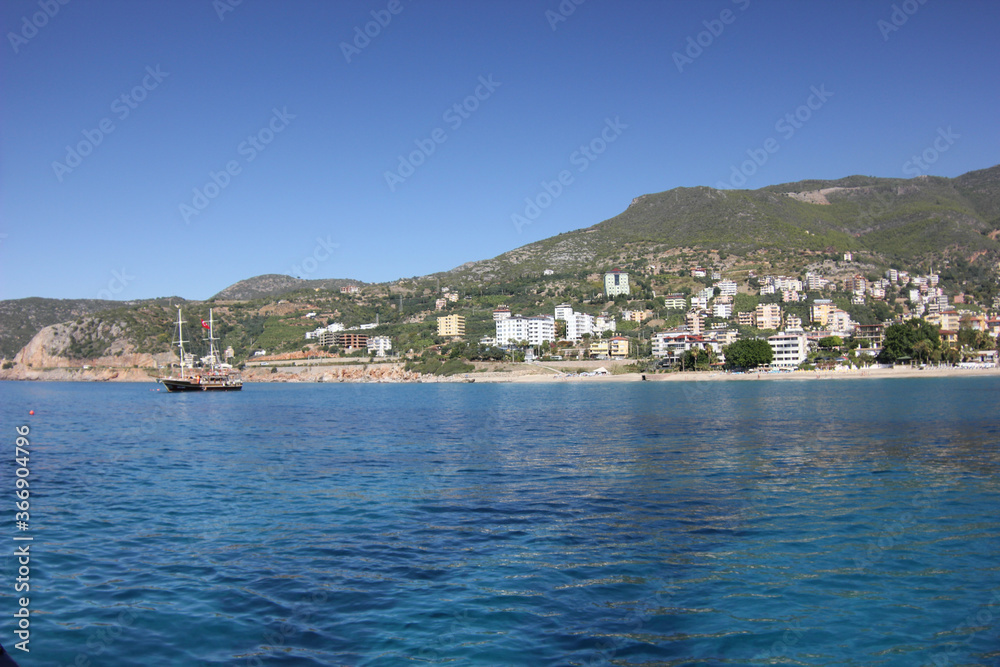 Alanya, TURKEY - August 10, 2013: Travel to Turkey. The waves of the Mediterranean Sea. Water surface. Mountains and hills on the coast of Turkey. Green hills. Port.