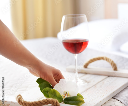 Hand decorating a tray with a glass of wine on the bed in the bedroom. Cozy tamosphere of spa and relaxation. photo