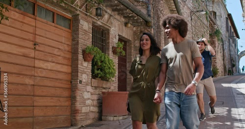 Four happy tourist walking through small street visiting rural town.Front follow. Group of multi ethnic people walking in old town.Friends vacation trip in Italy.4k slow motion