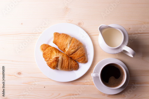 a white ceramic cup with black espresso, french croissant as breakfast or snack concept on rustic, natural texture wooden surface
