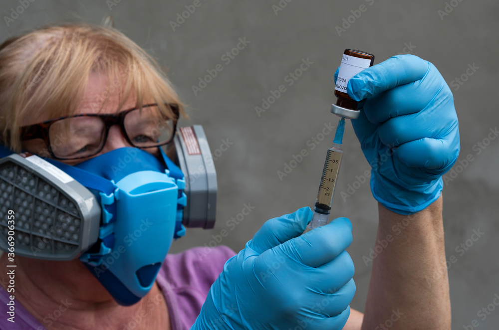In this photo illustration with Selective focus, a scientist wearing a mediated respirator and rubber gloves syringes liquid from a vial labeled Coronavirus vaccine In this photo illustration with Selective focus, a scientist wearing a mediated respirator and rubber gloves syringes liquid from a vial labeled Coronavirus vaccine