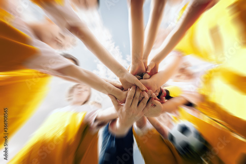 Low angle shot of a group of sports team forming a huddle with their hands. Sports team stacking hands together before the game. Sky with clouds in the background