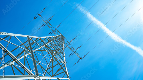 Electricity background - Voltage power lines / high voltage electric transmission tower with blue sky and shining sun