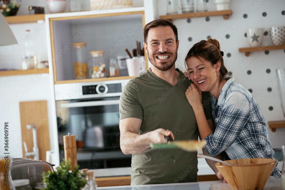 Fototapeta premium Young couple making pancakes together at home. Loving couple having fun while cooking. 
