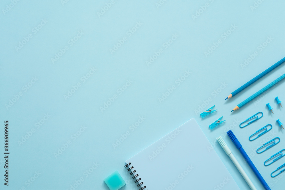 Education concept. Blue stationery set on the blue background. Top view of paper pins, notebook, felt-tip pens, eraser, paper clips and pencils. Knolling. Copy space.