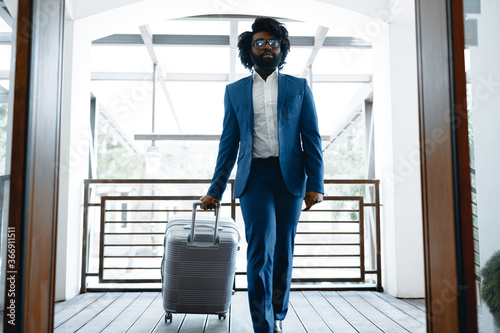 Black man in formal suit with packed suitcase entering hotel door