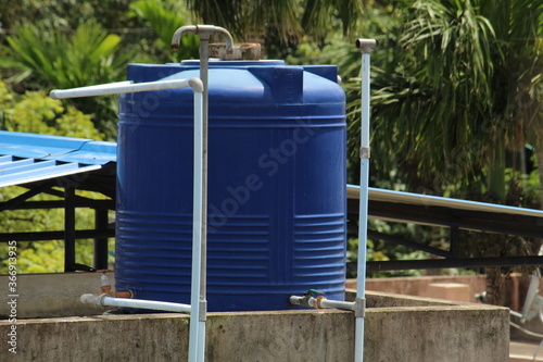Blue plastic made water tank and pipes on top of the roof as man made water reservoir.