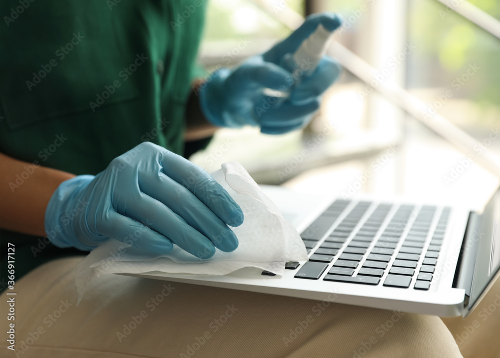 Woman in latex gloves cleaning laptop with wet wipe indoors, closeup Woman in latex gloves cleaning laptop with wet wipe indoors, closeup