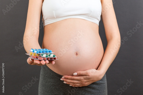 Close up of heap of blisters of pills in pregnant woman's hand at colorful background with copy space. Healthcare and treatment during pregnancy concept
