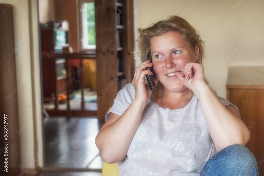 Portrait of a blond smiling woman talking on the phone at home.