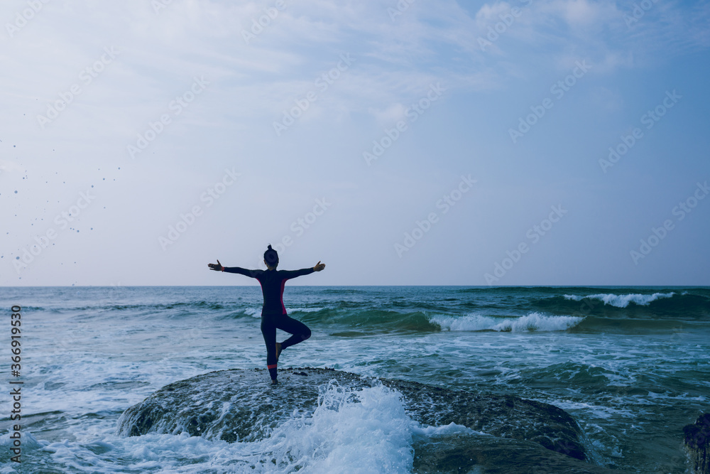 Woman practice yoga at seaside cliff edge facing the coming strong sea waves Woman practice yoga at seaside cliff edge facing the coming strong sea waves