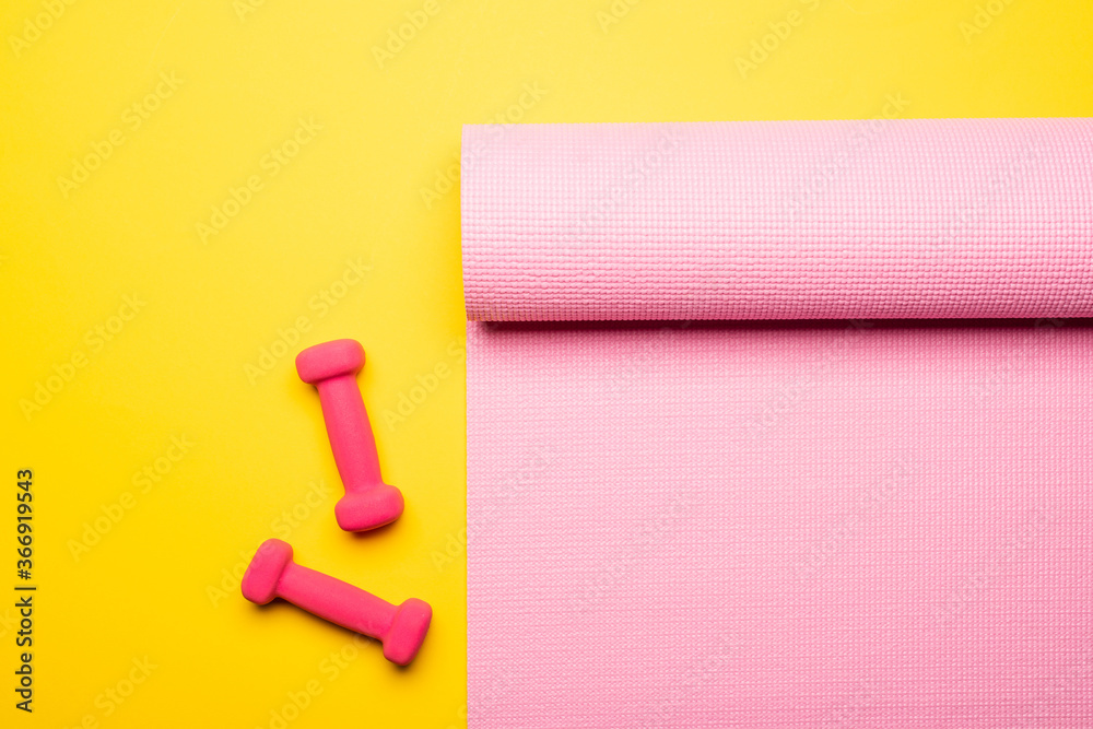 Obraz premium top view of pink fitness mat and dumbbells on yellow background
