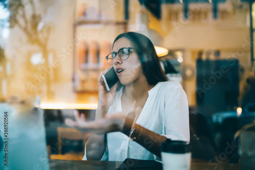 Tableau sur toile Angry caucasian female in eyewear sitting in cafeteria talking on mobile phone d