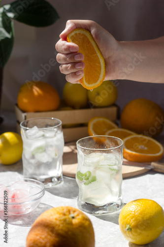 A glass filled with ice. From above, a woman's hand squeezes drops of orange juice into a glass