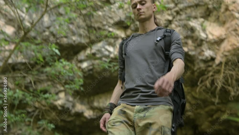 An attractive man with a backpack goes under a rock in the woods in the afternoon and looks around. Mountain single tourism An attractive man with a backpack goes under a rock in the woods in the afternoon and looks around. Mountain single tourism