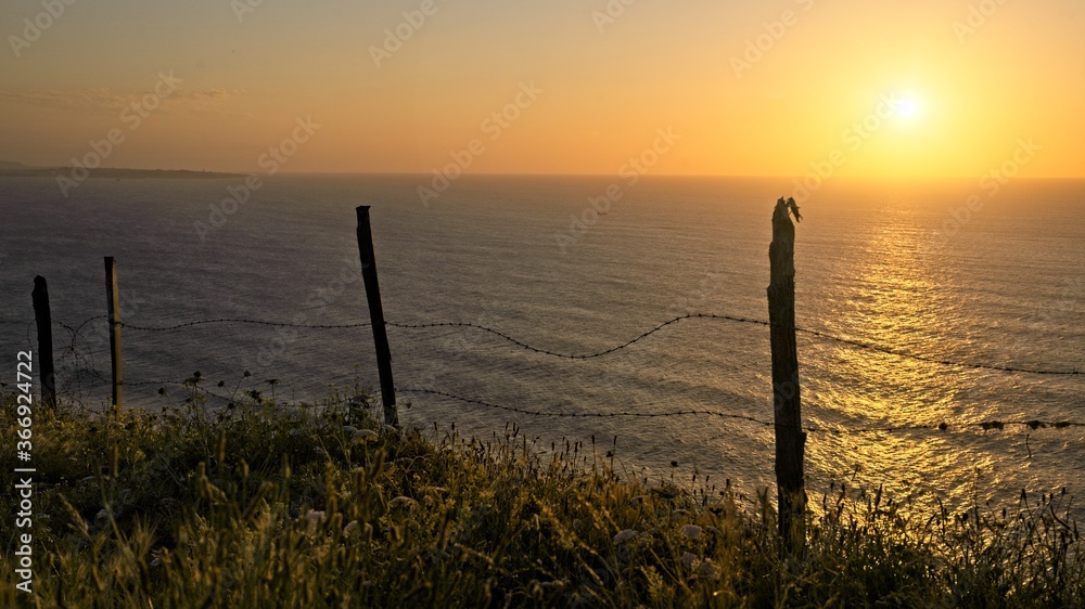 Obraz premium Barbed wire in front of the ocean at sunset 