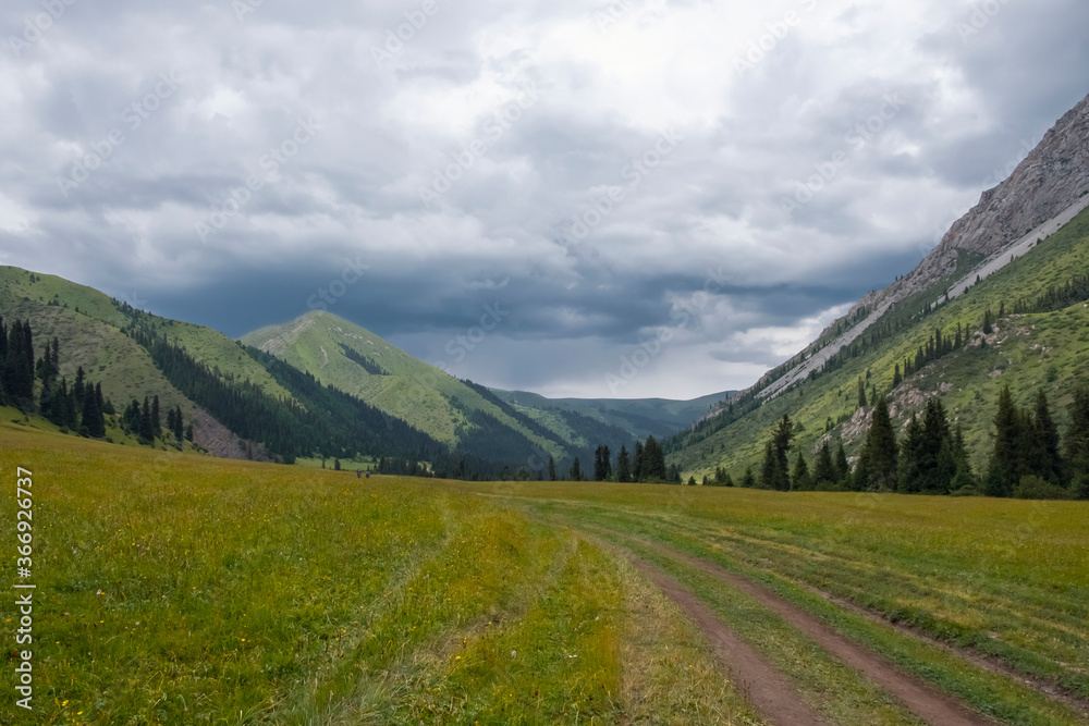 Obraz premium Green mountain valley with clouds. Adventure travel. Outdoor landscape. Summer vacation travel concept. Kazakhstan mountains, Tekes river valley. Tourism in Kazakhstan concept.