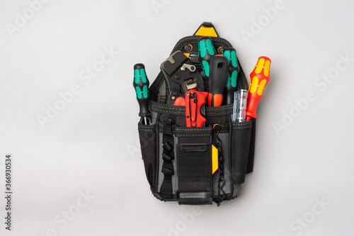 Fototapeta Naklejka Na Ścianę i Meble -  A black electrician's or Builder's bag with tools on a gray table. Bag with construction tools: screwdrivers, knife, crimping on a gray background. Top view with space for text