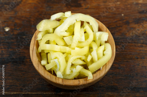 Sliced raw yellow peppers in a bowl on a wooden background. Vegetable, ingredient and staple food.