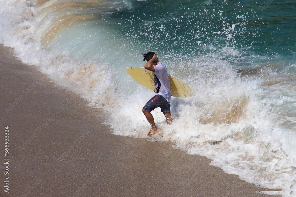 Skim boarder coming in from the surf after skimming on his board. Skim boarder coming in from the surf after skimming on his board.